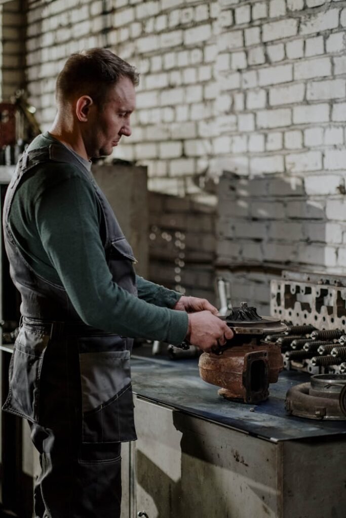 Mechanic focused on repairing a car engine part in an indoor workshop setting.